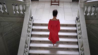 Unrecognizable woman in red dress on high heels climbs a large staircase