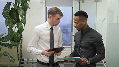 Male african worker is talking to his caucasian boss about the report in the office.