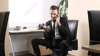 Work out in the office, man in a suit does an exercise for the biceps while sitting in the office and speaking on the