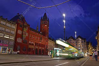 Night view of red Basel Town Hall at Marktplatz with a moving green tram on the designated track, Switzerland