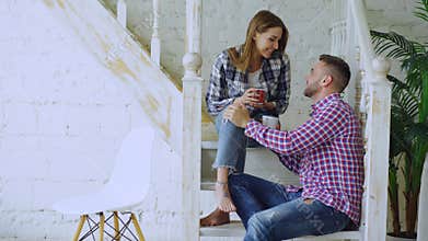 Young happy and loving couple drink tea and talking while sitting on stairs in living room at home