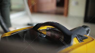 The woman cleans the house and vacuums the floor. Opinion from the vacuum cleaner with the background blurred.