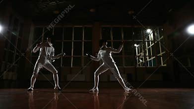 Young man and woman dressed in costumes for fencing practice in the sports hall. Back on the background it is snowing