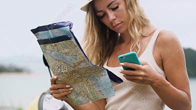 Blonde girl in a hat, sits on a bike and looks at the phone and a map, looks at the route in Asia
