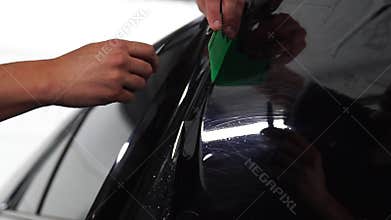 Master installs tint film for car glass with hairdryer and spatula with glare of light. Concept tinting