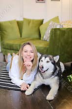 Woman lying on floor with malamute near sofa.