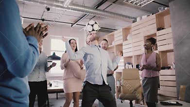 Happy Caucasian manager juggles football on head. Cheerful multiethnic employees celebrate success in office slow motion