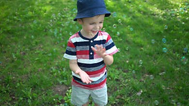 Happy little boy blowing soap bubbles in park