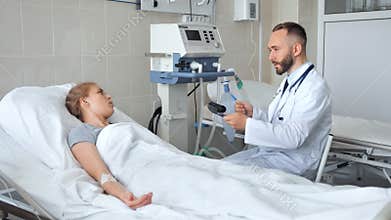 Doctor sitting near hospital bed and discussing with young female patient