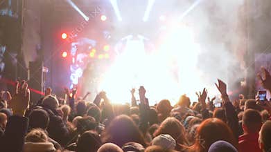 Jumping fans with hands up delight of live music of rock band on bright scene