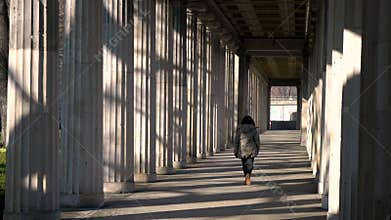 Young woman teenage girl mixed race female wearing camouflage jacket, walking through columns passageway during the d