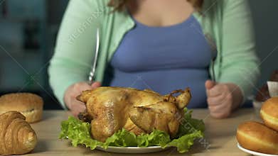 Plump lady sharpening knife against fork, getting ready to eat big roast chicken