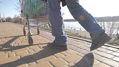Rear view of homeless man`s legs walking with cart
