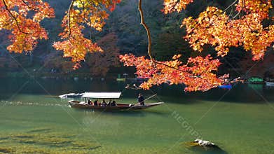 Unidentified tourists on wooden boat enjoy autumn colors along Hozu gawa river at Arashiyama in Kyoto