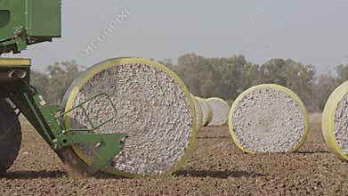 Cotton picker harvesting a cotton field creating large cotton bales