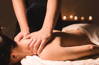 Men`s hands make a therapeutic neck massage for a girl lying on a massage couch in a massage spa with dark lighting