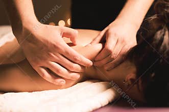 Men`s hands make a therapeutic neck massage for a girl lying on a massage couch in a massage spa with dark lighting