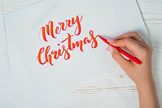 Merry Christmas congratulations. Calligrapher writes with red ink on white card. Calligraphy. Ornament font. The art of