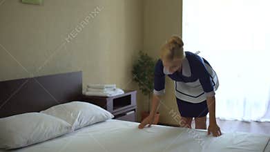 Beautiful chambermaid smoothing bed sheets, satisfied with new bleachers action