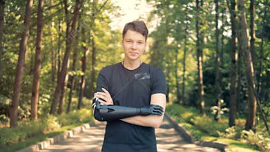 Disabled man with bionic prosthesis stands, crossing his hands. Human with a robot arm.
