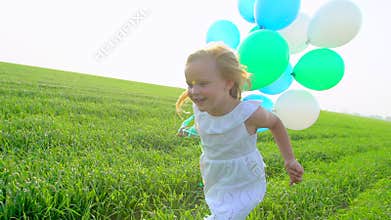 Little girl in a dress running through green wheat field with balloons in hand. Child, kid running in garden and