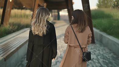 Rear view of two young women walking and talking, inviting the viewer to follow