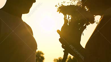 Man giving woman flowers and they kissing on sunset background, romantic moment