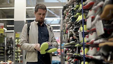 Male customer is taking sport shoes from rack in a sport hypermarket