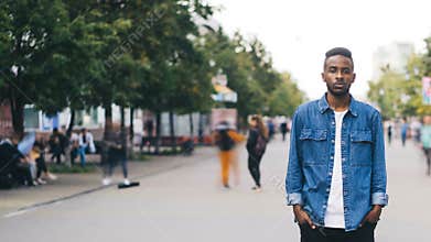 Time-lapse of lonely African American guy student standing in pedestrian street in big city with hands in pockets and