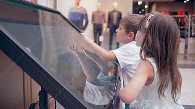 Modern little boy with girl uses Touchscreen of self-service machine For search information about location of halls and