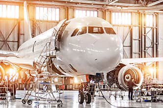 Passenger commercial airplane on maintenance of engine turbo jet and fuselage repair in airport hangar. Aircraft with open hood on