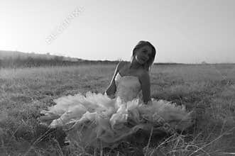 Beautiful bride in designer wedding gown seated in field at sunrise