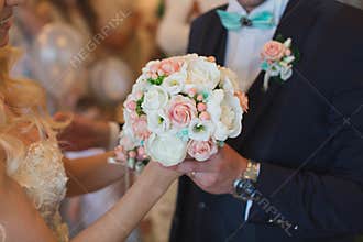 Groom in a suit gives the bride a white and peach wedding bouquet.