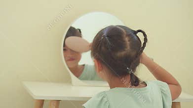 Asian little girl brushing her bangs hair with comb and smiling in the mirror of dressing table