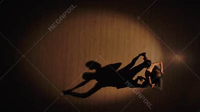 Top view of a couple of ballroom dancers dancing Argentine tango elements on a parquet floor with dancing shadows