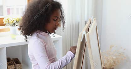Little African girl drawing on white board with crayon
