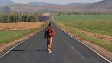 Hipster hitchhiker tourist traveler man walking along long road, hitchhiking summer