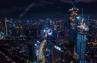 Aerial night view of high rise skyscrapers under construction and modern city center with multi lane highway in Jakarta