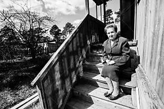 An Old woman sitting on the porch of house. Black and white photo.
