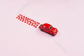 Valentine\'s Day background. Red retro toy car  red hearts confetti  on pink background. Valentines day creative concept.