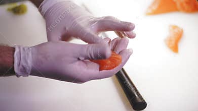 Traditional Japanese food. Sushi preparation. close-up. Sushi Chef, in disposable gloves, is preparing sushi with salmon