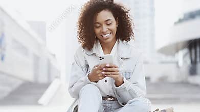 Young smiling woman using smartphone in a city. Student girl texting mobile phone outdoor.