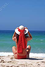 Woman in red bikini sitting on beach adjusting hat