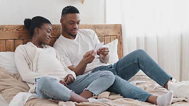 Happy African American couple married husband and wife pregnant afro black ethnic family future parents sitting on bed