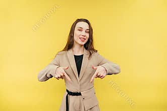 Cheerful woman in a suit stands on a yellow background with a smile on his face points his fingers down at the copy space and