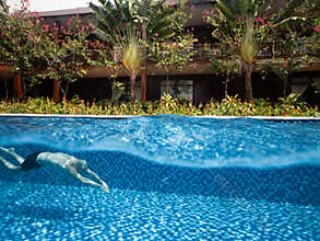 Tropical Villa with flowers and trees and pristine swimming pool with a man swimming.