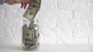 hand putting a dollar bill in a savings jar with a white label