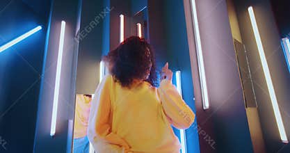 Wide angle positive african american black woman in yellow hoodie dancing in night club backlit with purple and blue