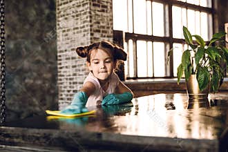 A beautiful little girl in rubber gloves does the cleaning, rags the dust from the table.