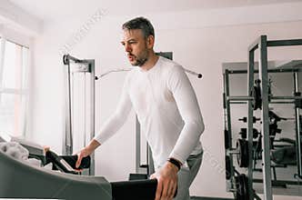 a tired man in a sweat-soaked T-shirt runs on a treadmill in a sports club. cardio workout